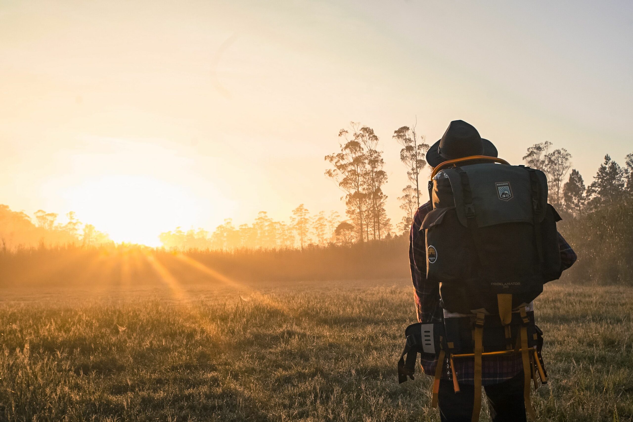 A lone backpacker gazes at a sunrise over a foggy field, embracing adventure.