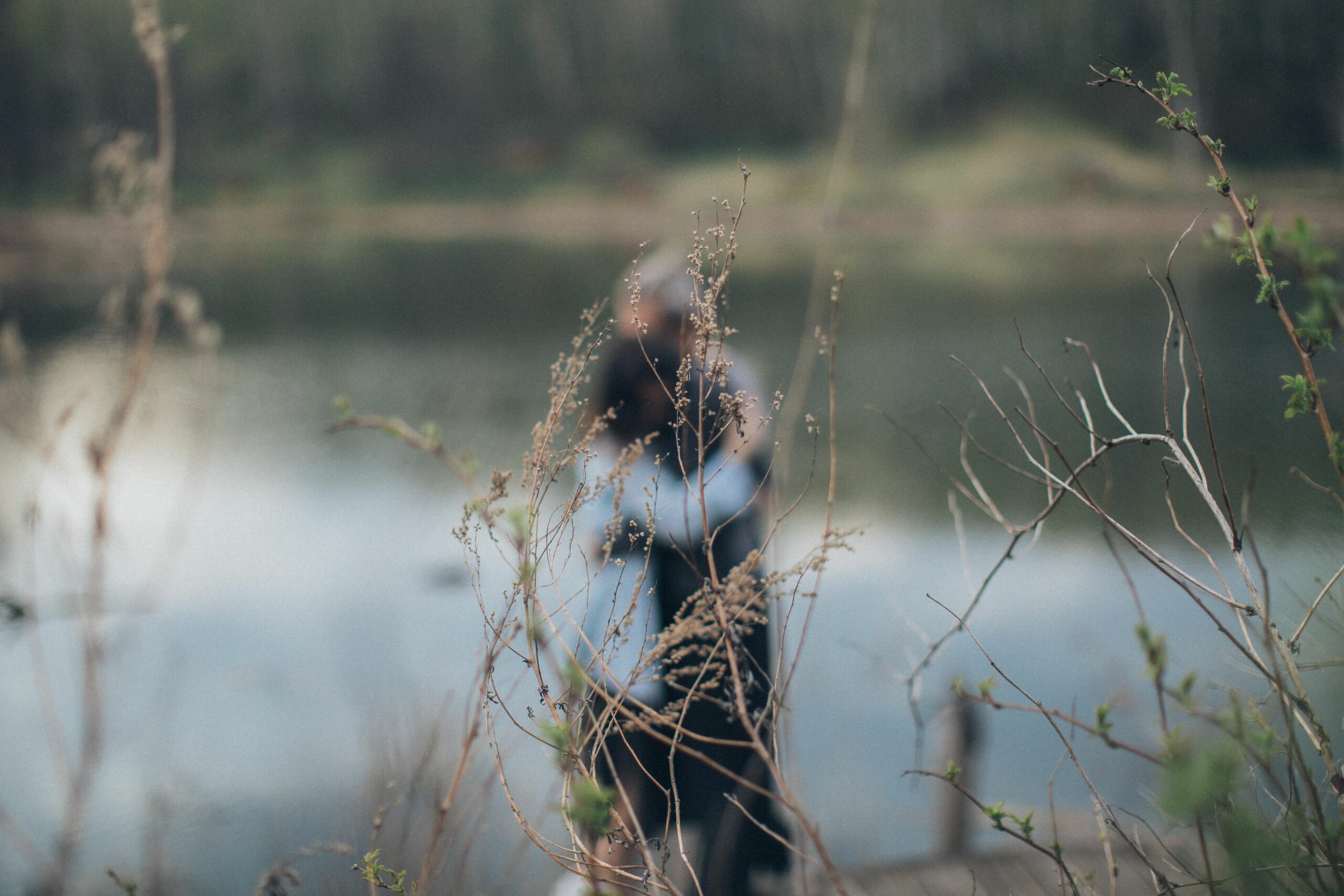 Side view of unrecognizable blurred calm couple hugging each other while standing near pond